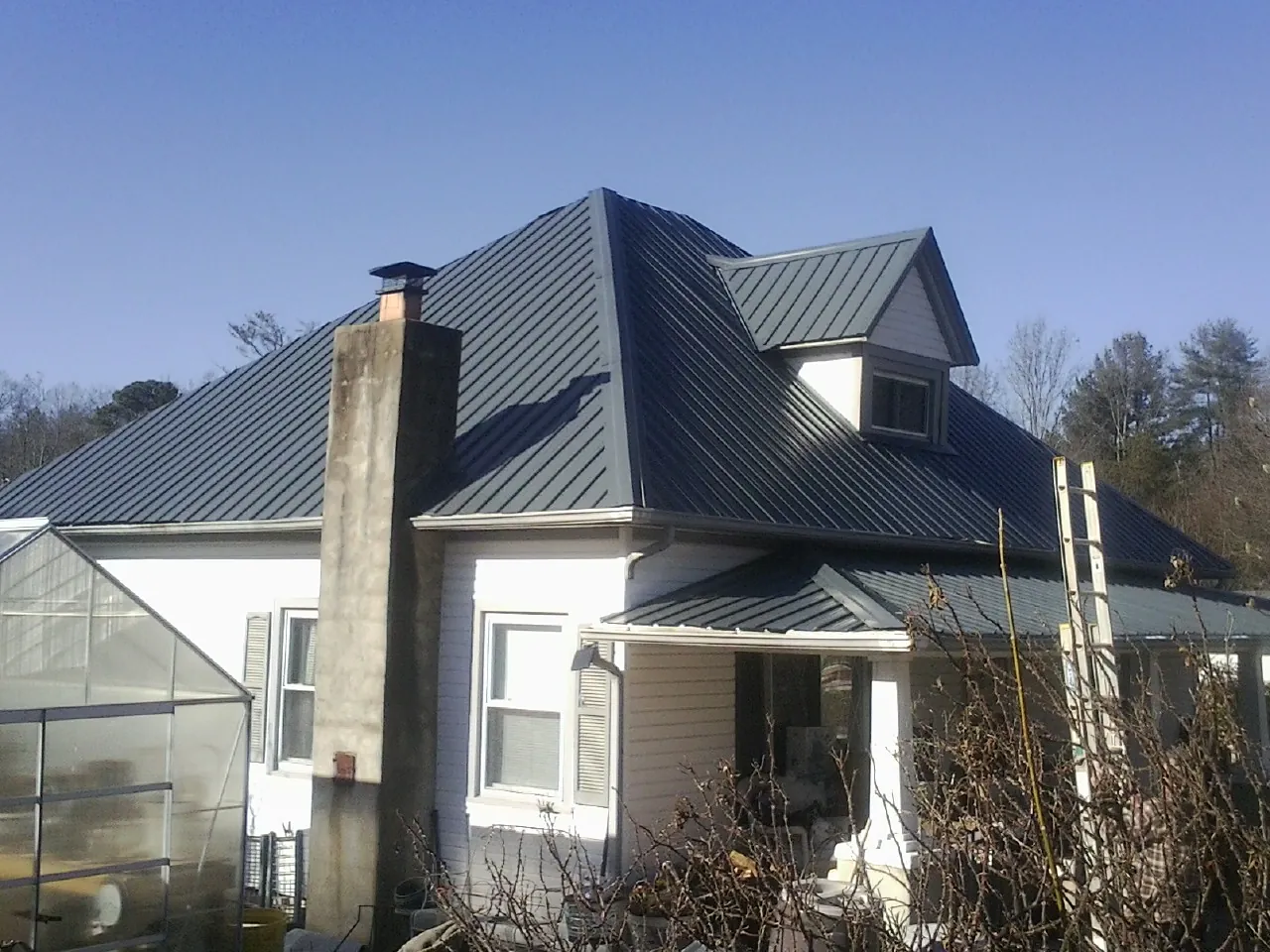 Dark blue standing seam metal roof on a white farmhouse with dormer — Slate & Tile Roof Repair by Roofing Brothers in Rockwell