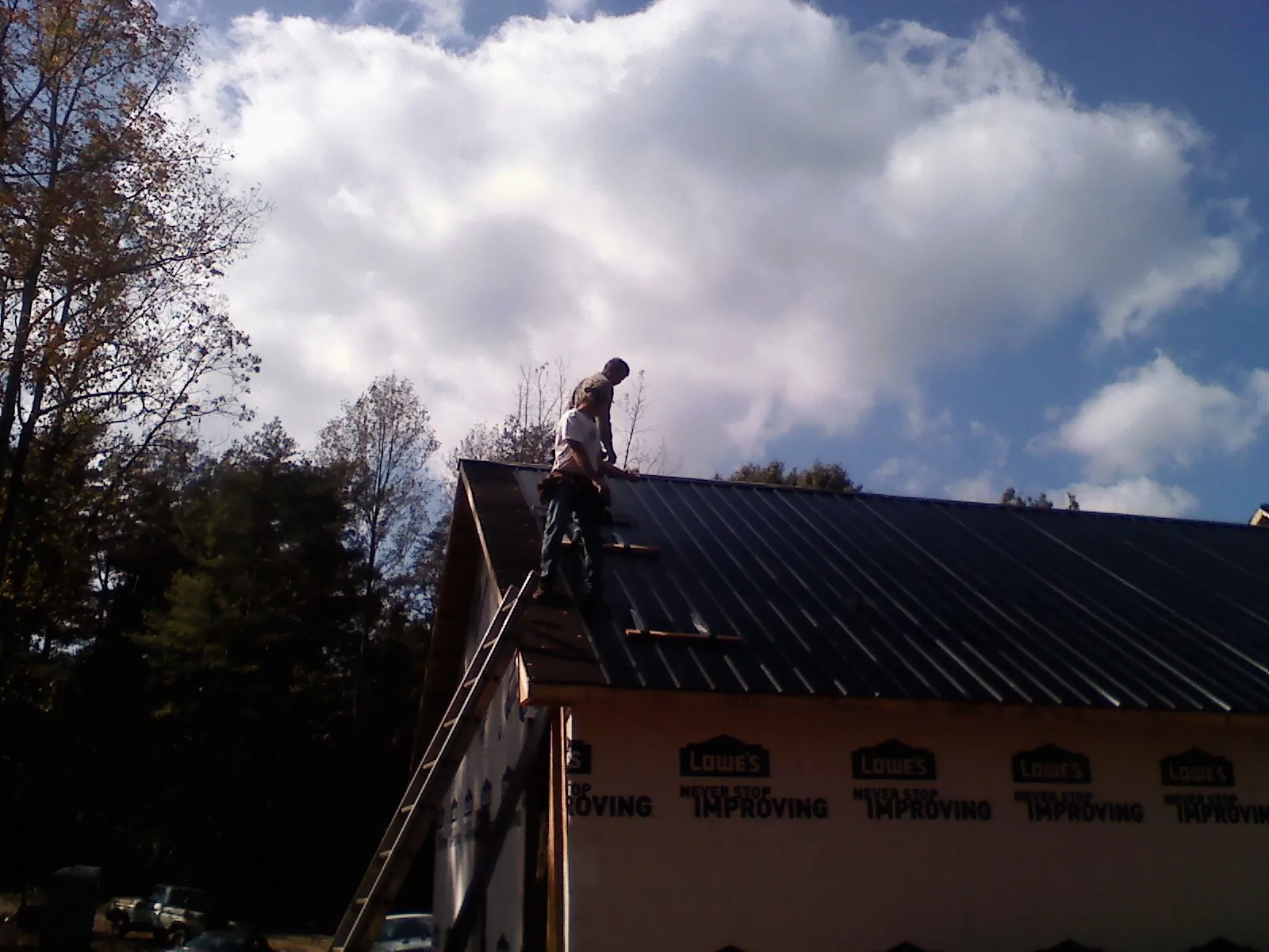 Roofer fastening dark metal panels high against a cloudy sky, from a Roof Inspection job in Rockwell