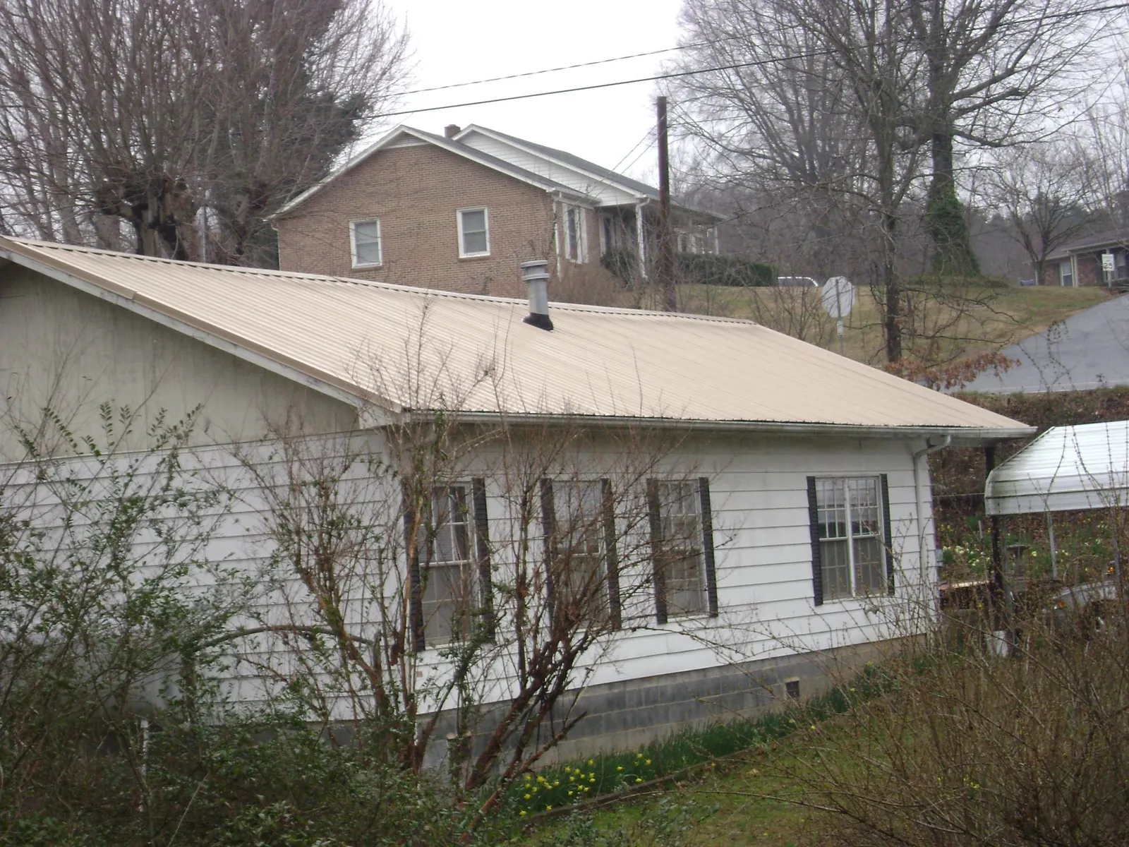 Tan metal roof on a white sided house set into a hillside — Commercial Roofing by Roofing Brothers in Rockwell